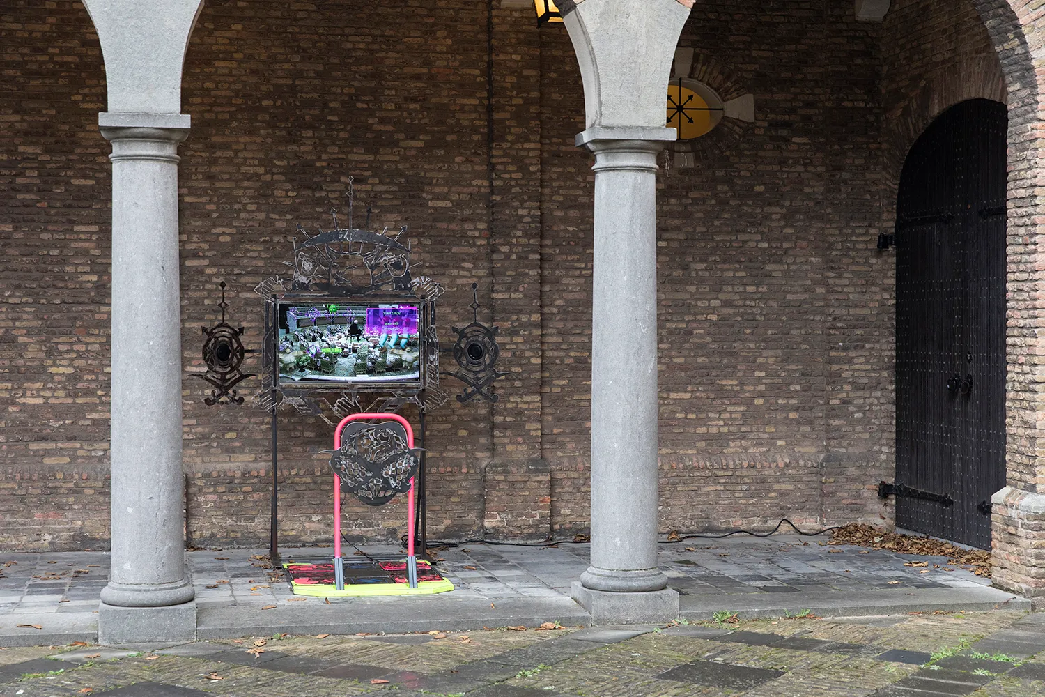 A screen with a dancepad placed outside under the arch of a building