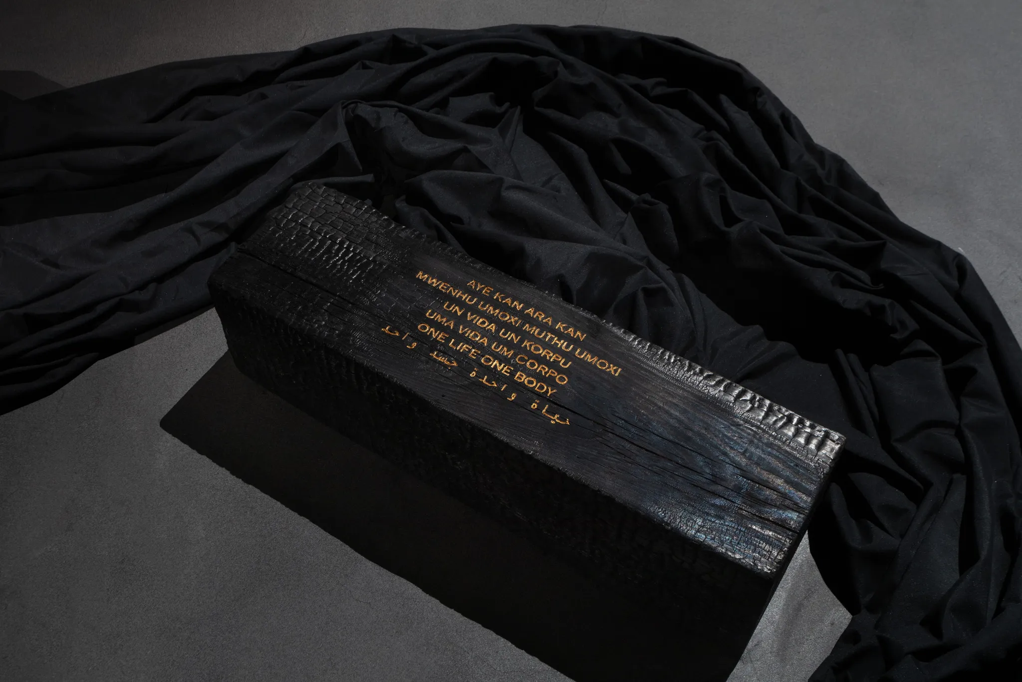 A black wood log with the inscription 'one life one body' engraved in gold colour