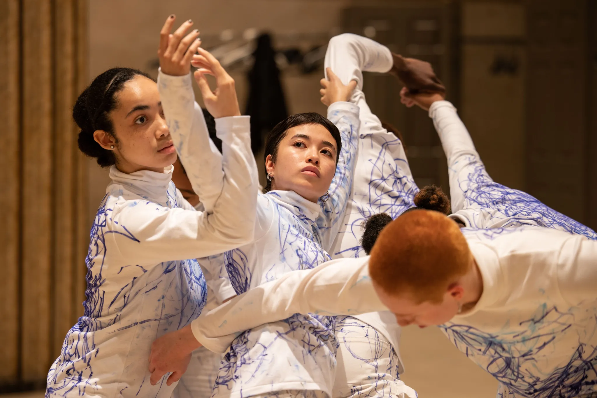 Five performers in a cohesive formation, connecting hands and gracefully moving as they prepare to embrace.