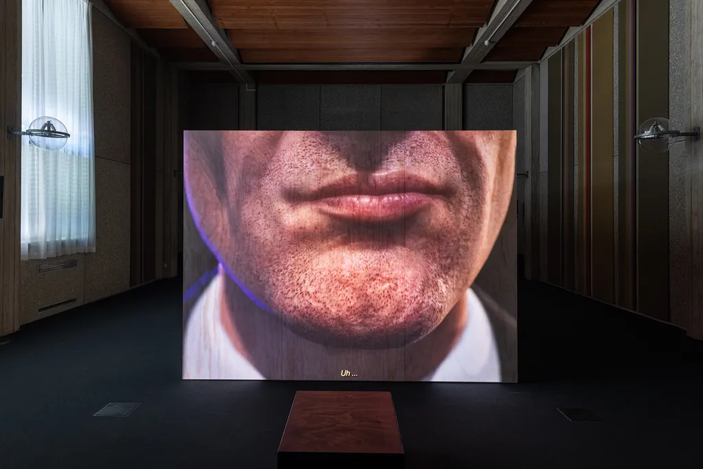 Projectie van een close-up digitaal personage (onderste gezicht) op een houten kist in een voormalige rechtszaal