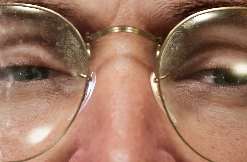 Close up of a digital rendition of a caucasian person’s face with golden framed glasses stained with finger marks