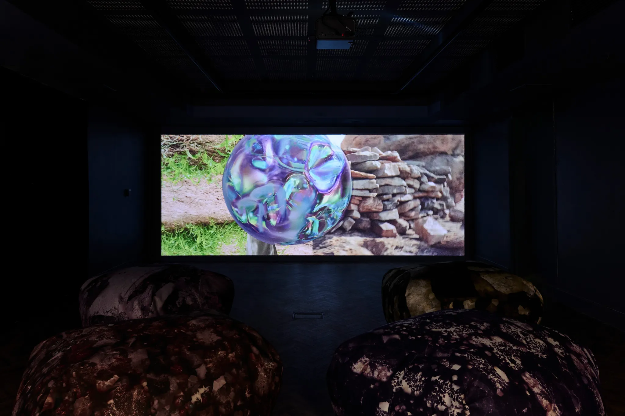 Four rock-like bean bag chairs in front of a screen with a video work