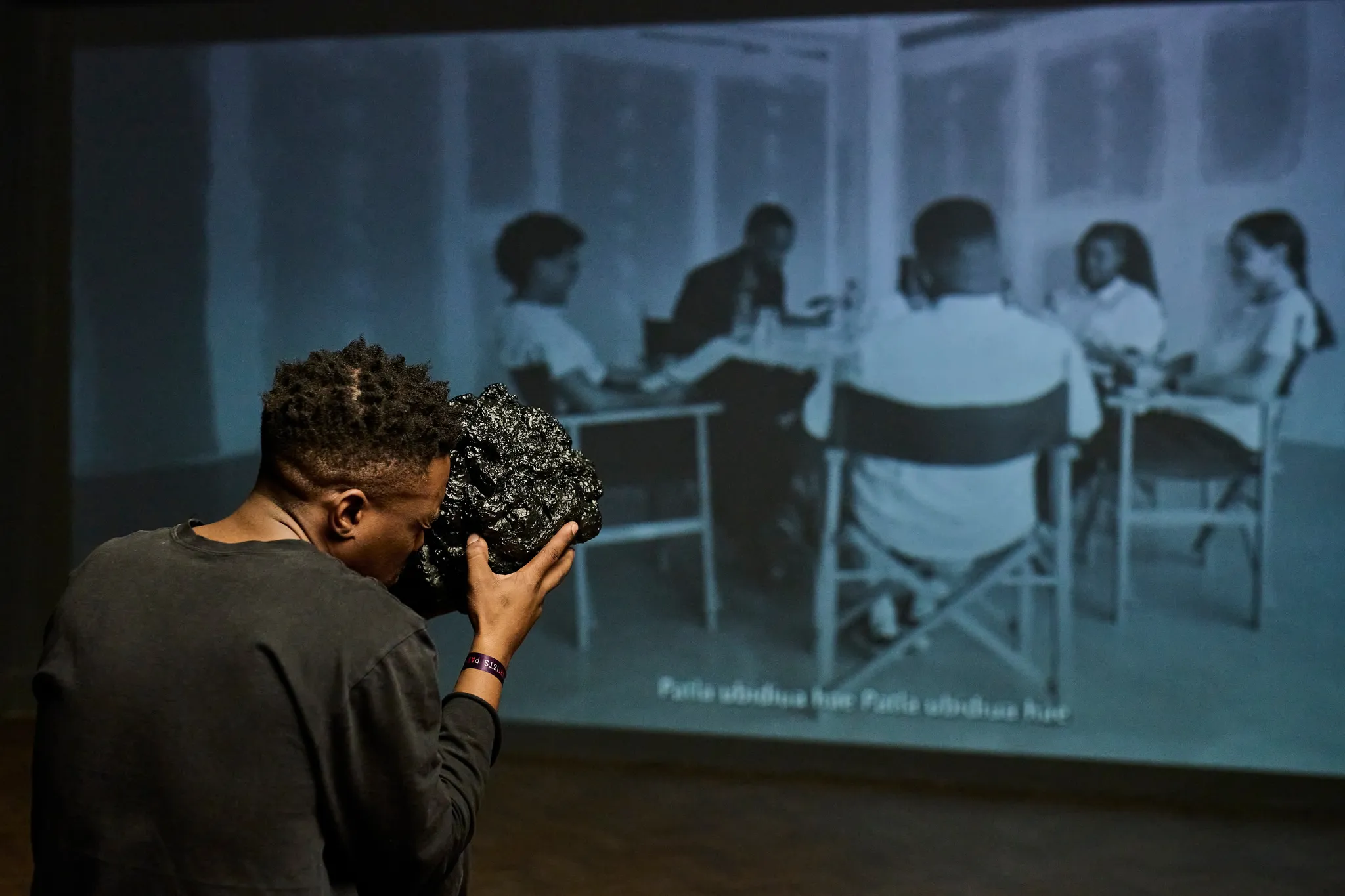 A person using a shiny black rock as a viewing device to watch the projection of a black & white film