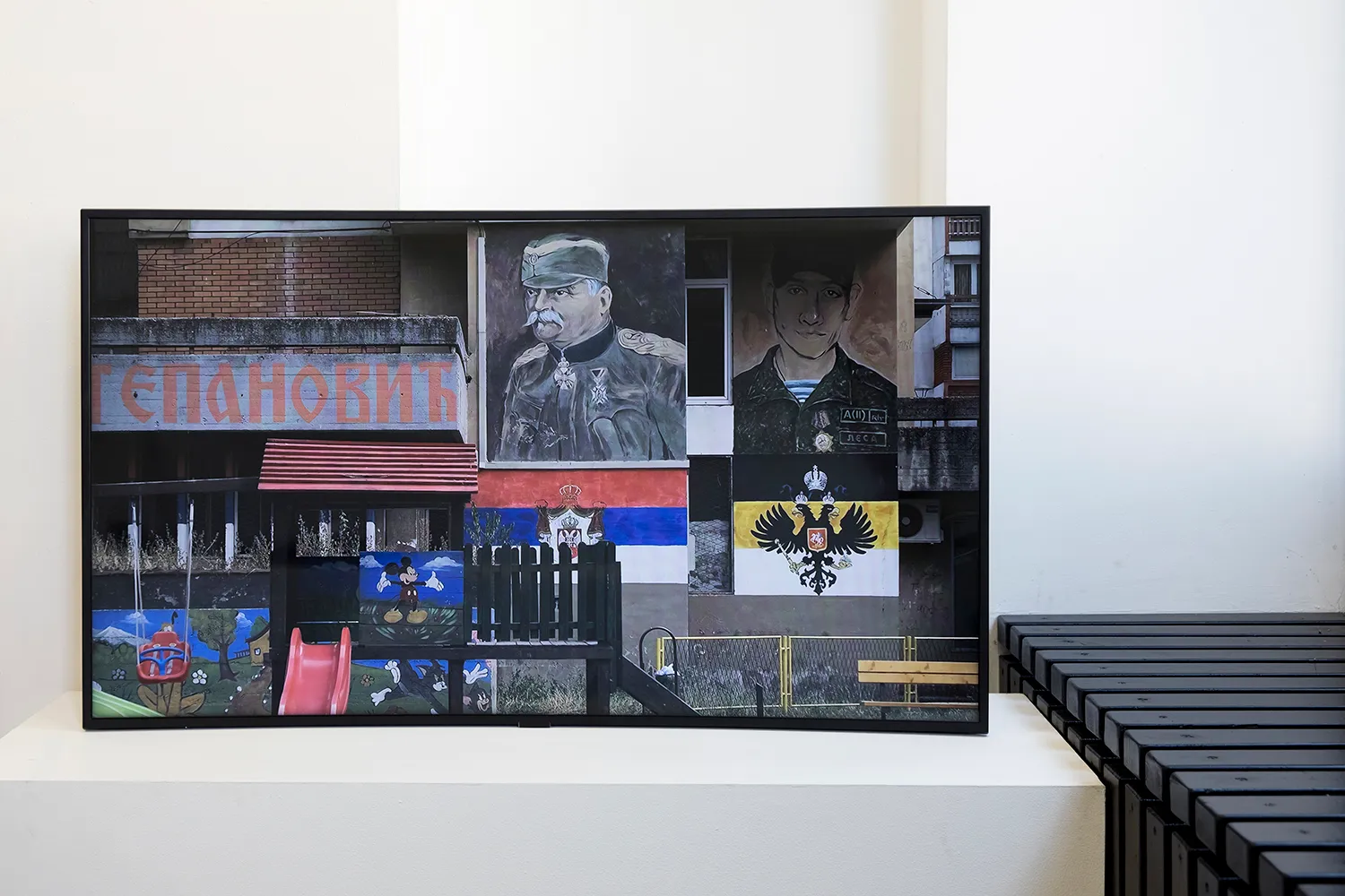 A screen showing the image of an outdoor children playground with painted soldiers, flags, Mickey Mouse and Cyrillic writings on the walls