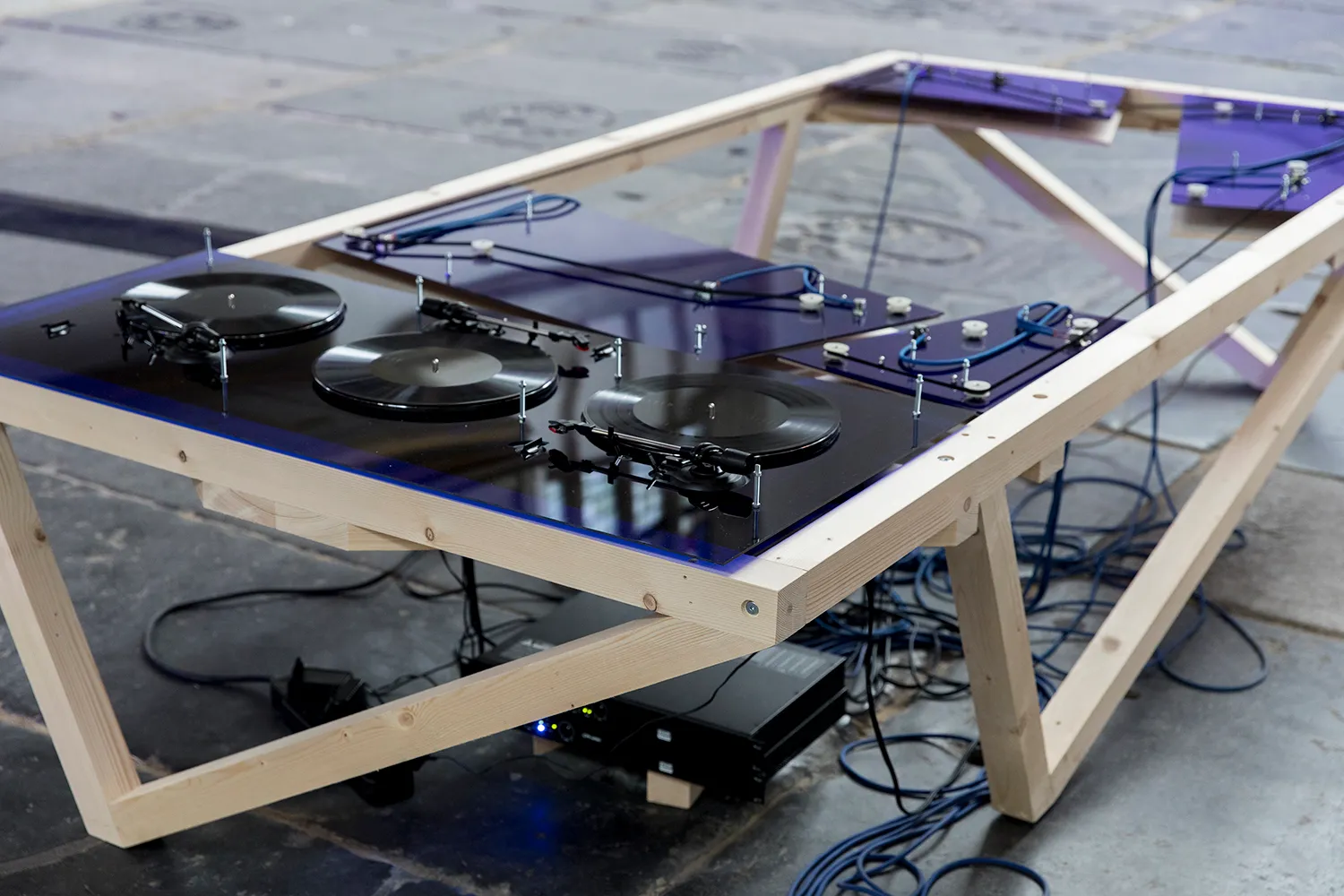 3 LP's spelen op een op maat gemaakte speler, gemaakt van donkerblauw plexiglas, hout en een netwerk van kabels.