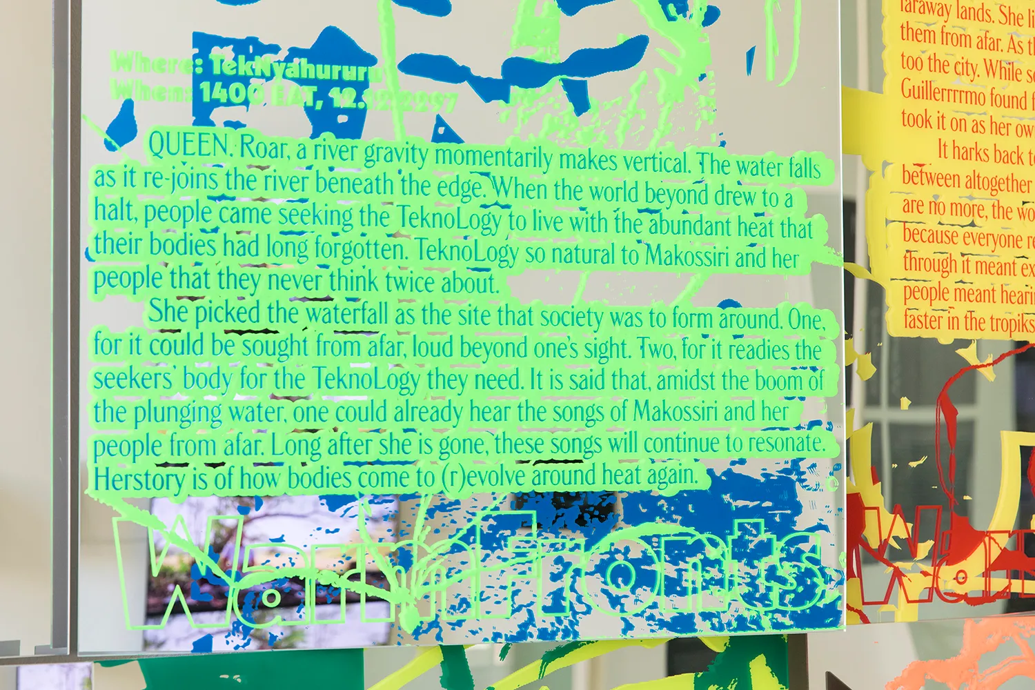 Close up of a mirror with printed text in green and blue "Queen. Roar, a river gravity momentarily vertical..."