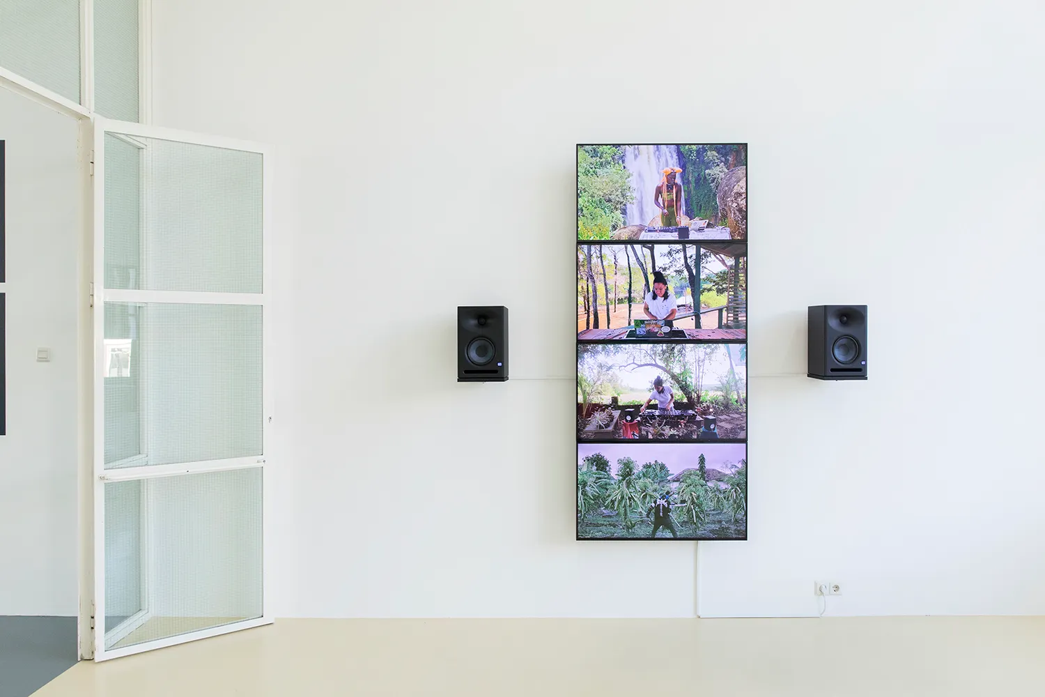 4 flatscreens die een verticale streep vormen op de muur met 2 speakers. Op elk scherm treedt een andere DJ op, voor een tropische achtergrond.