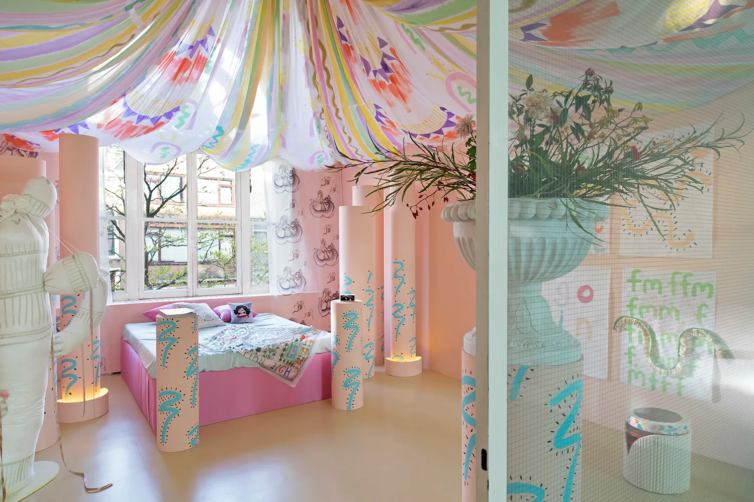 A flamboyant pink room with a bed, painted columns, flowers and draping hanging from the ceiling