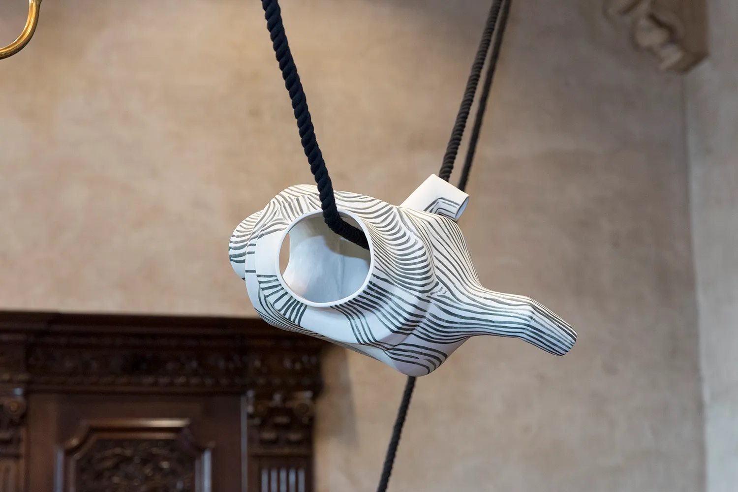 A white ceramic vessel with painted black line, hanging from a black rope