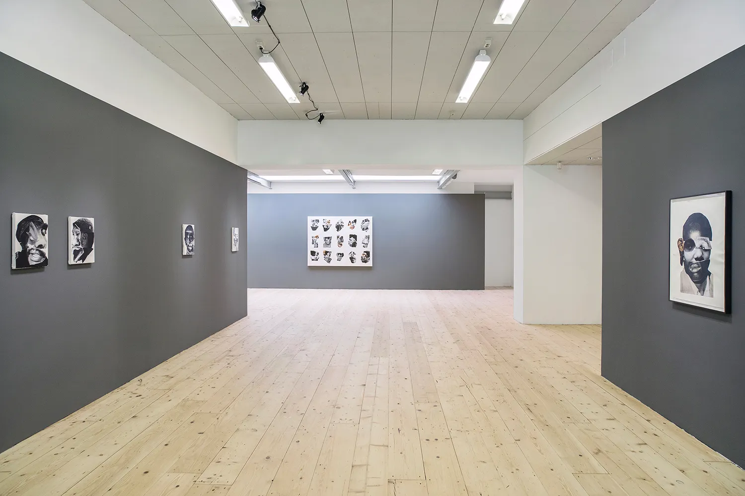 View of the gallery space with works on canvas by the artist hanging on dark grey walls