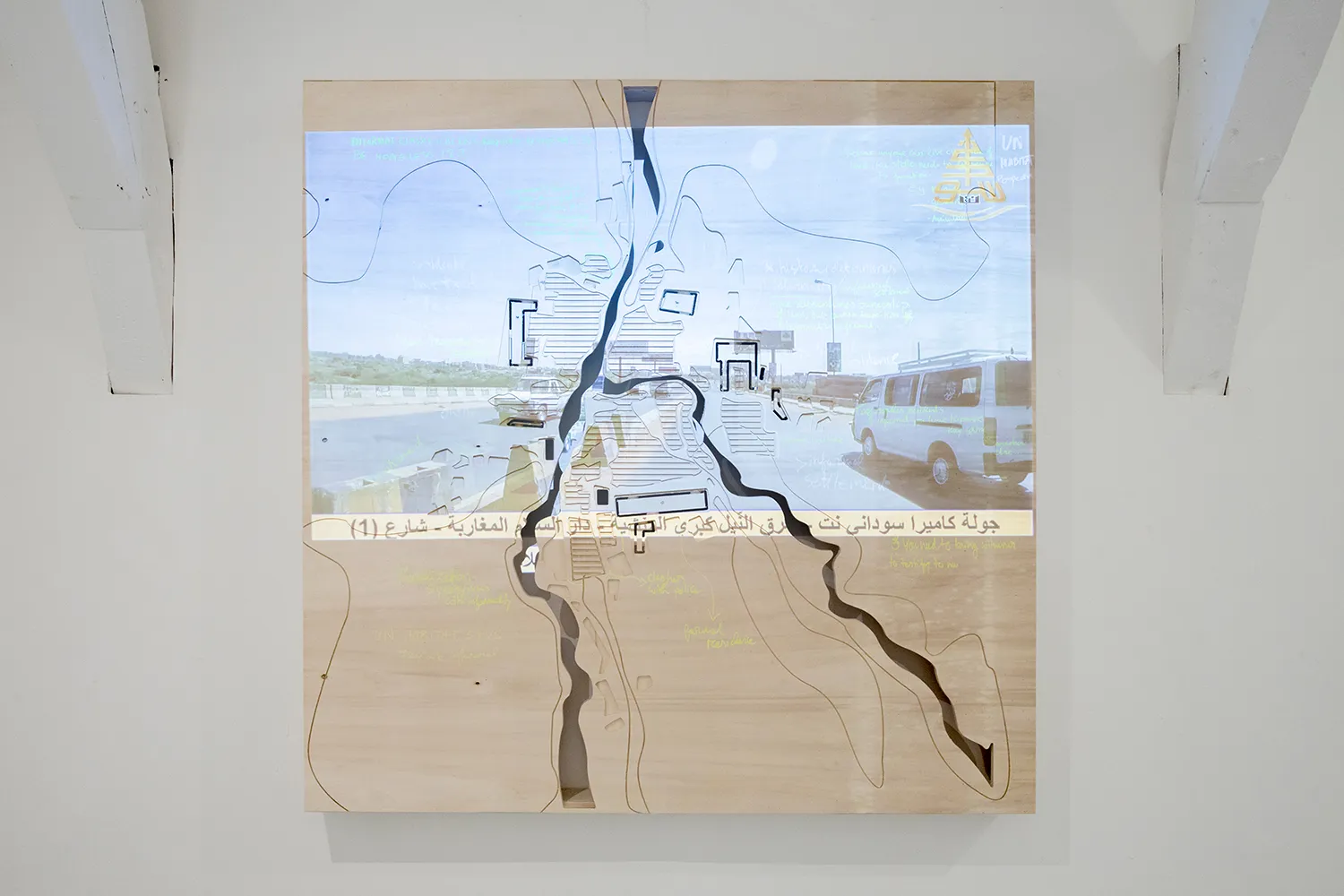 Een kaart gesneden in een houten plank met verschillende fluorescerende aantekeningen, waarop een afbeelding van een weg met auto's wordt geprojecteerd.