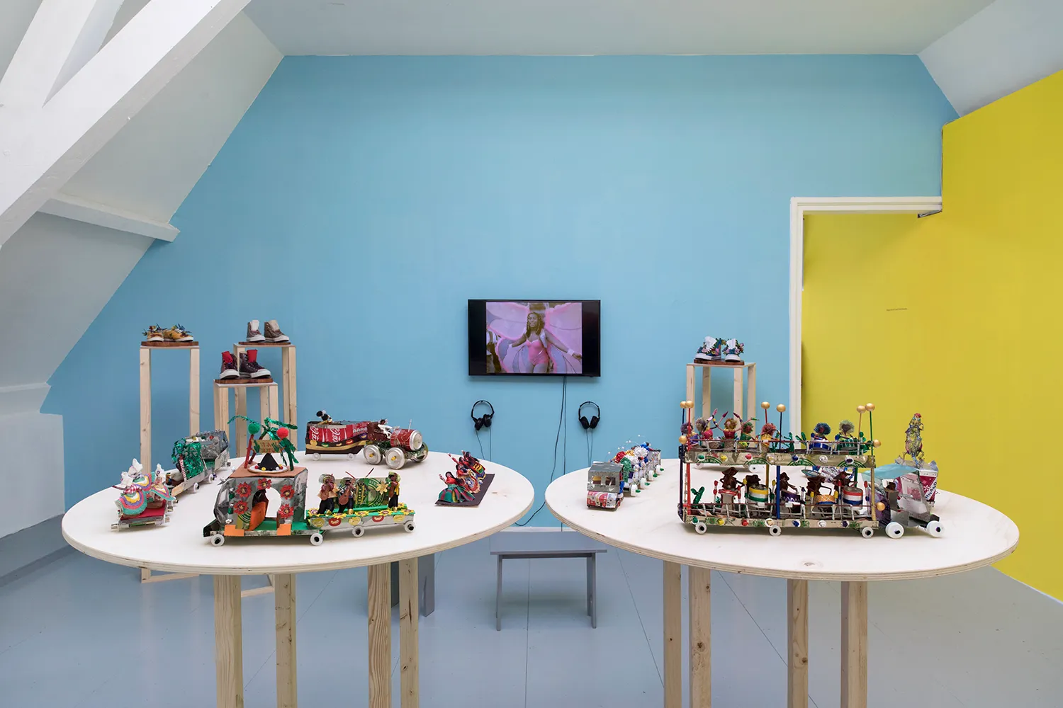 Overview with several miniatures of carnaval procession, 4 pairs of shoes on pedestal and a screen with the video of a carnival queen in a pink outfit