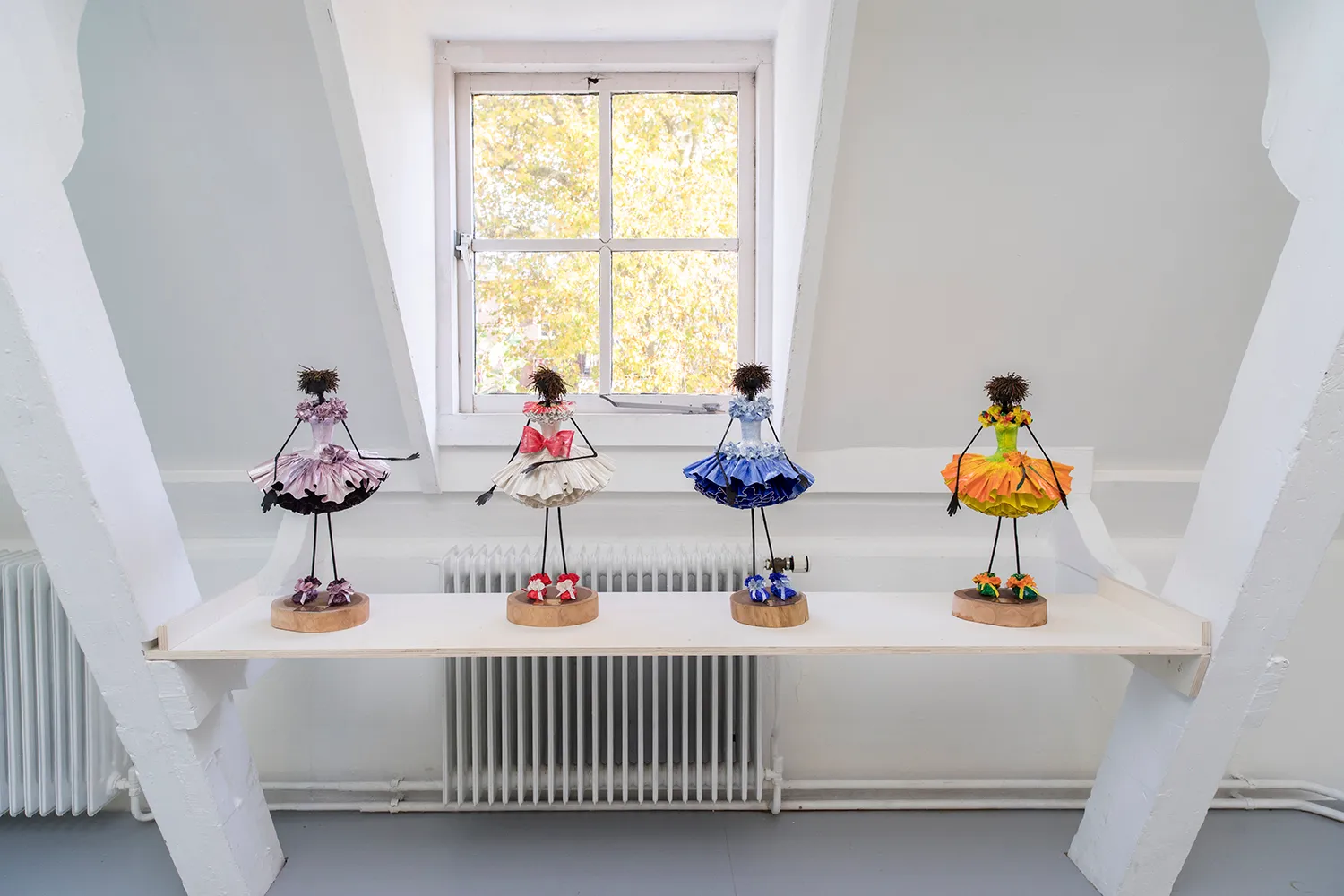 Four little black dolls with thin arms and legs wearing colourful tutu's and shoes