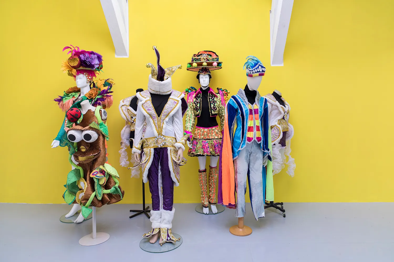 7 mannequins with carnival costumes standing in front of a yellow wall