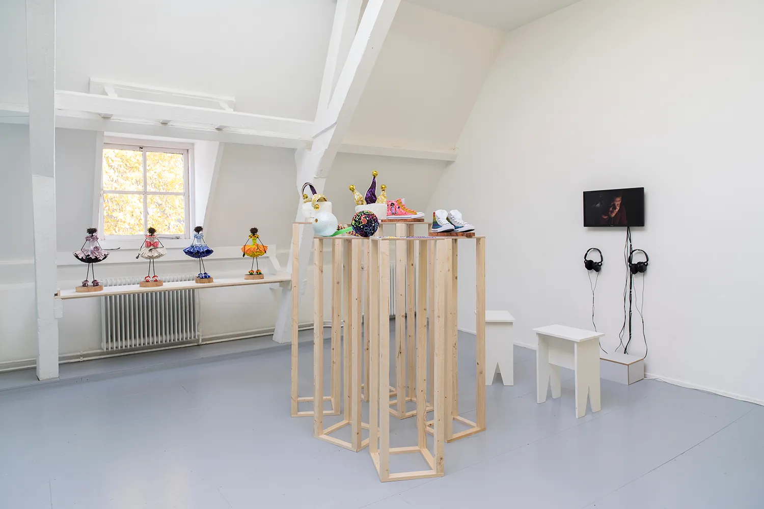An exhibition space with pedestals with shoes and carnival hats, a shelve with dolls and a screen on a wall
