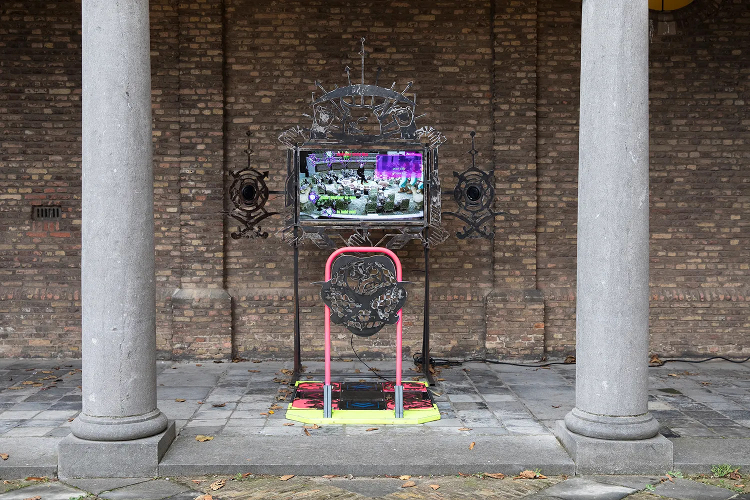 A screen mounted on a custom-made stand with metal ornaments, with a colourful dance pad in front