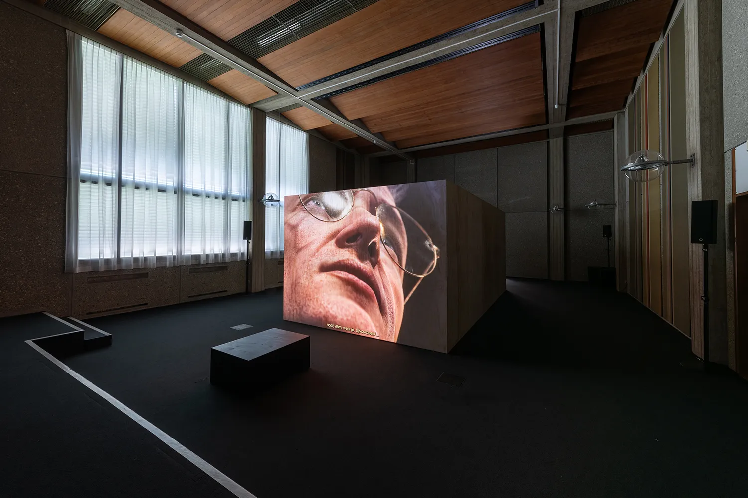 Projection of a close up digital character (lower face) on a wooden box in a former courtroom