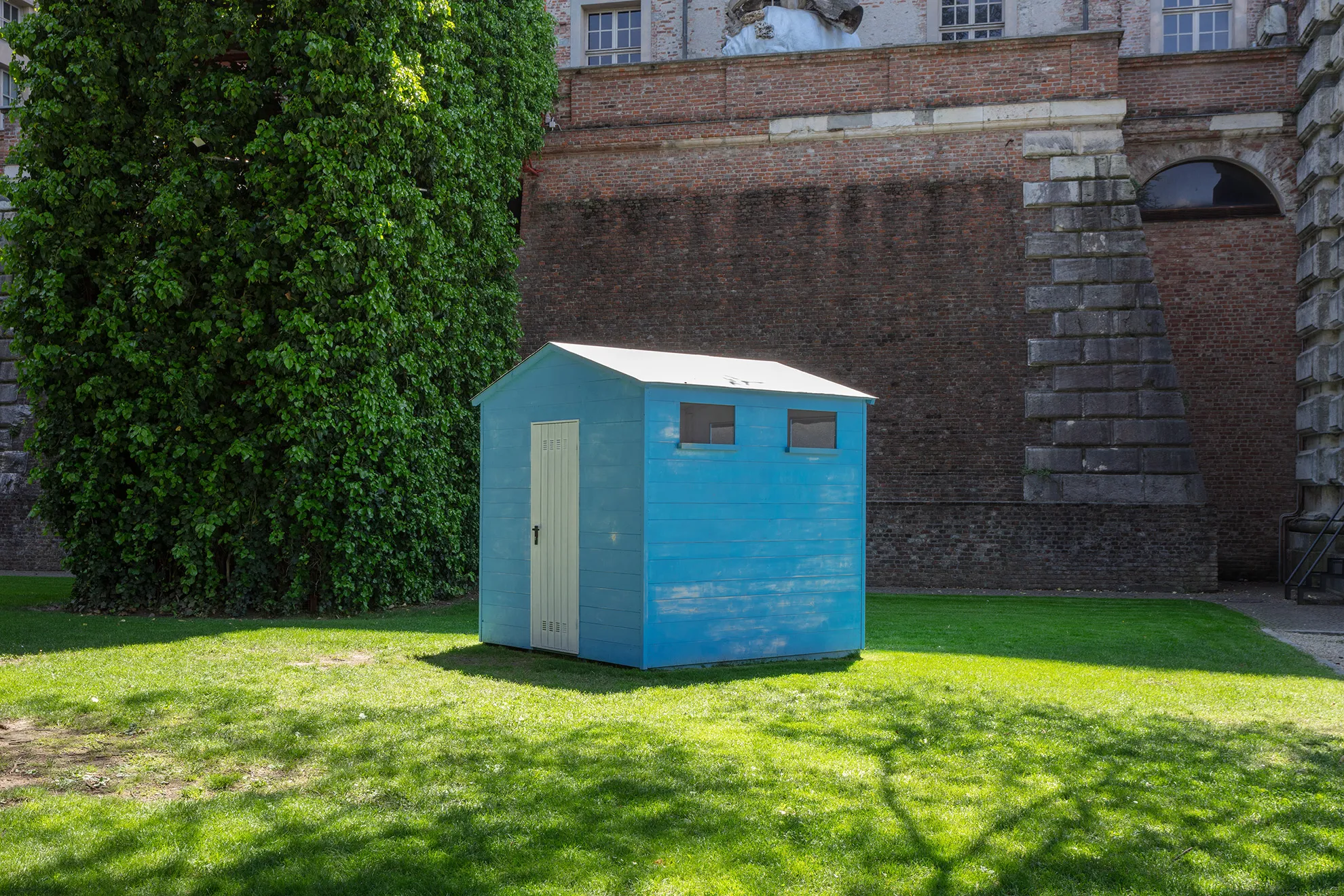 A blue wooden beach cabin on a sunny green lawn