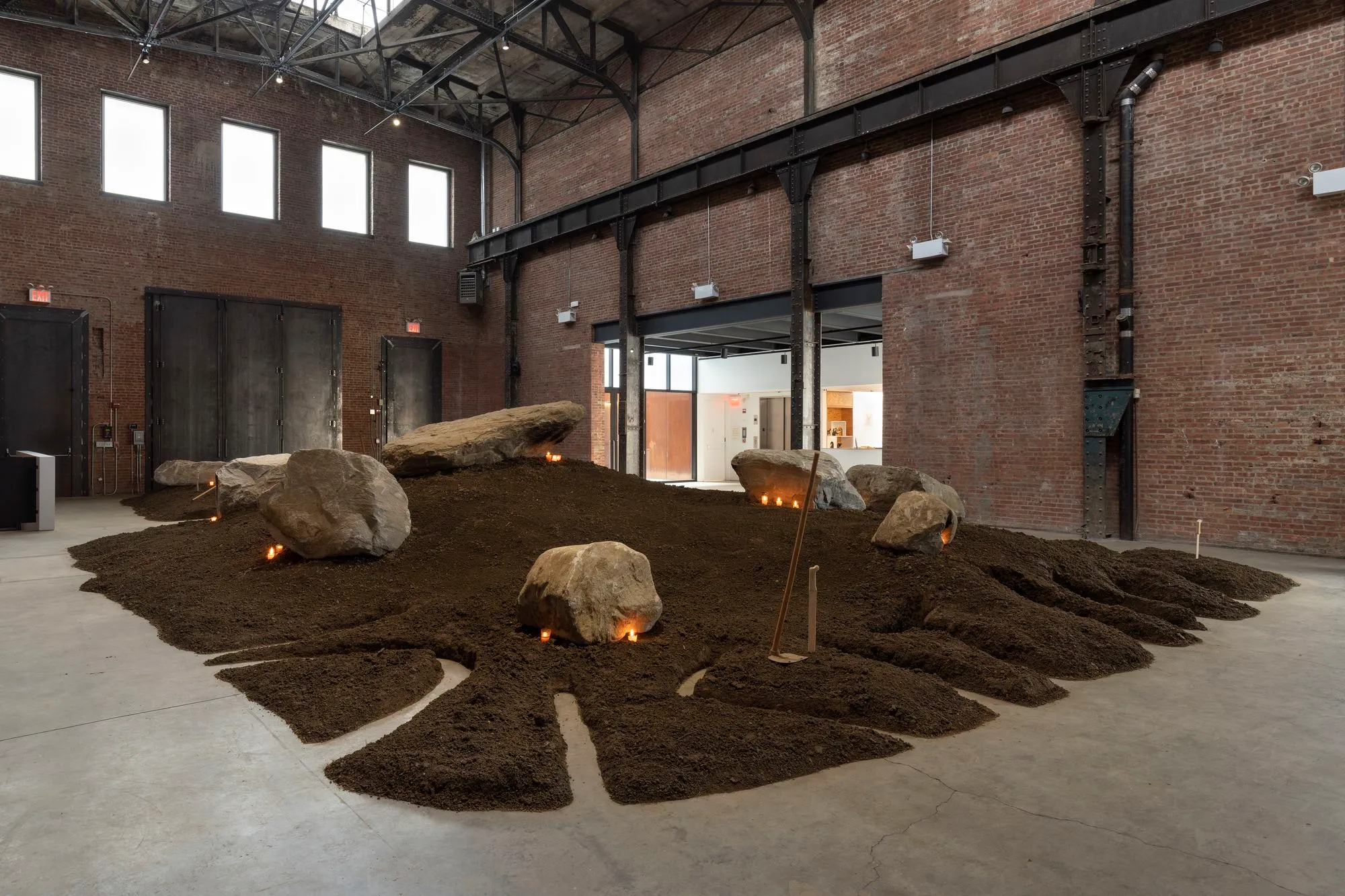 An installation of brown soil, rocks and fire inside a red-bricked warehouse