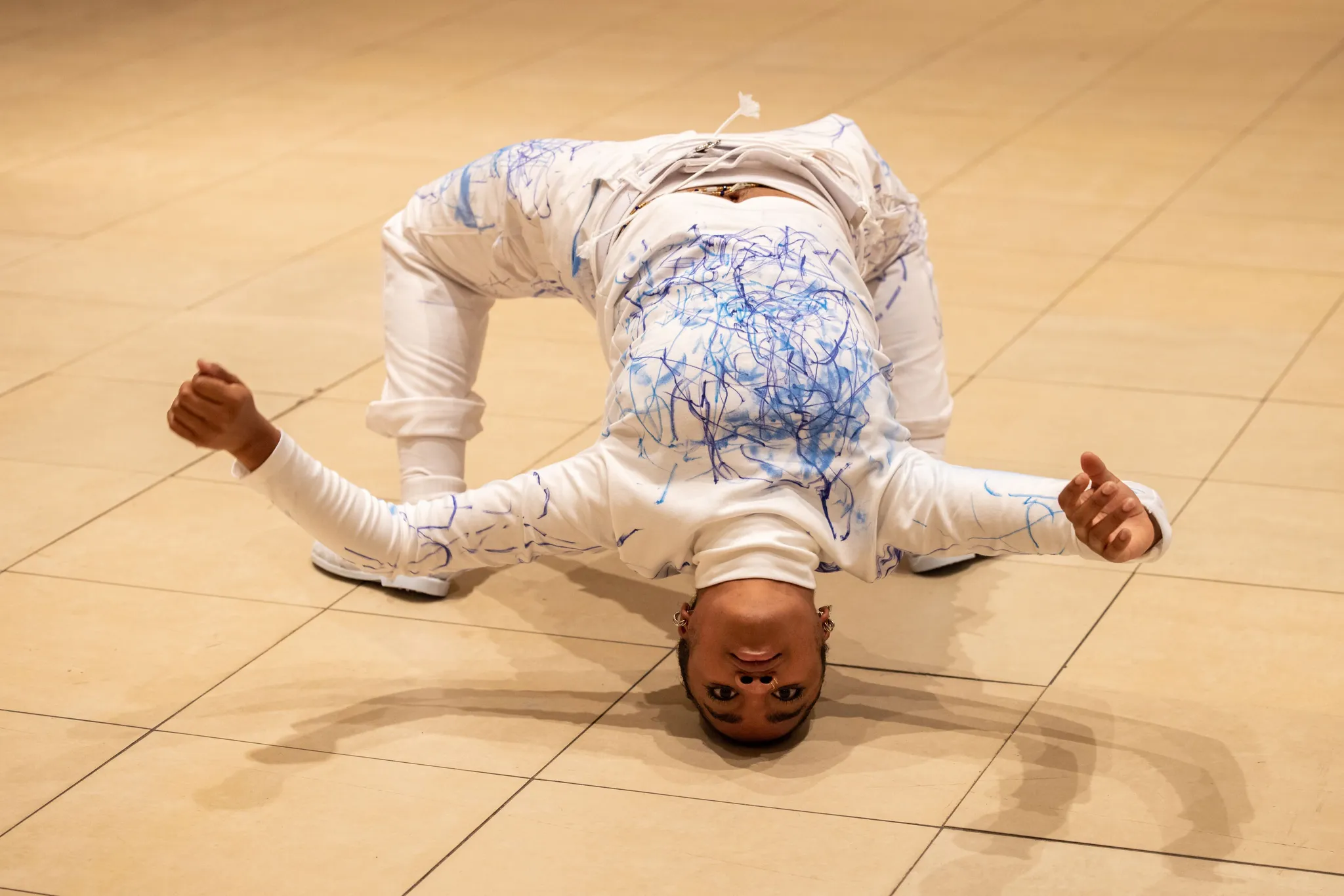 Performer strekt zich uit in een brughouding op de vloer en kijkt intens naar de camera