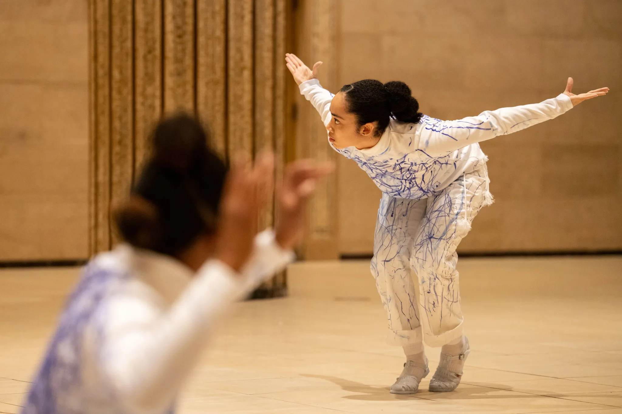 Elevated performer on tiptoes with outstretched arms, while another artist in the foreground adds a dynamic, blurred effect