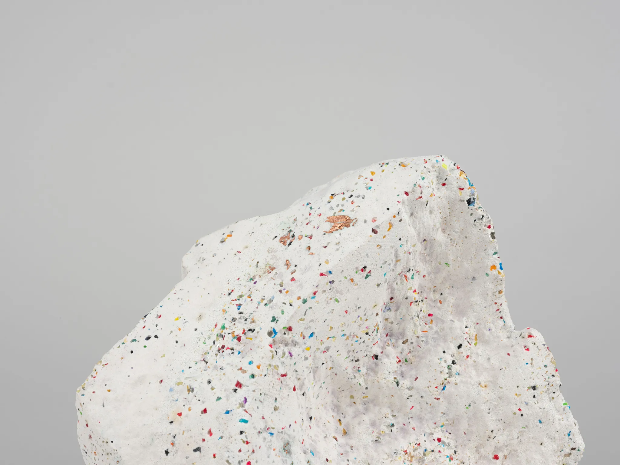 A white porous stone with colorful dots, photographed against a white background