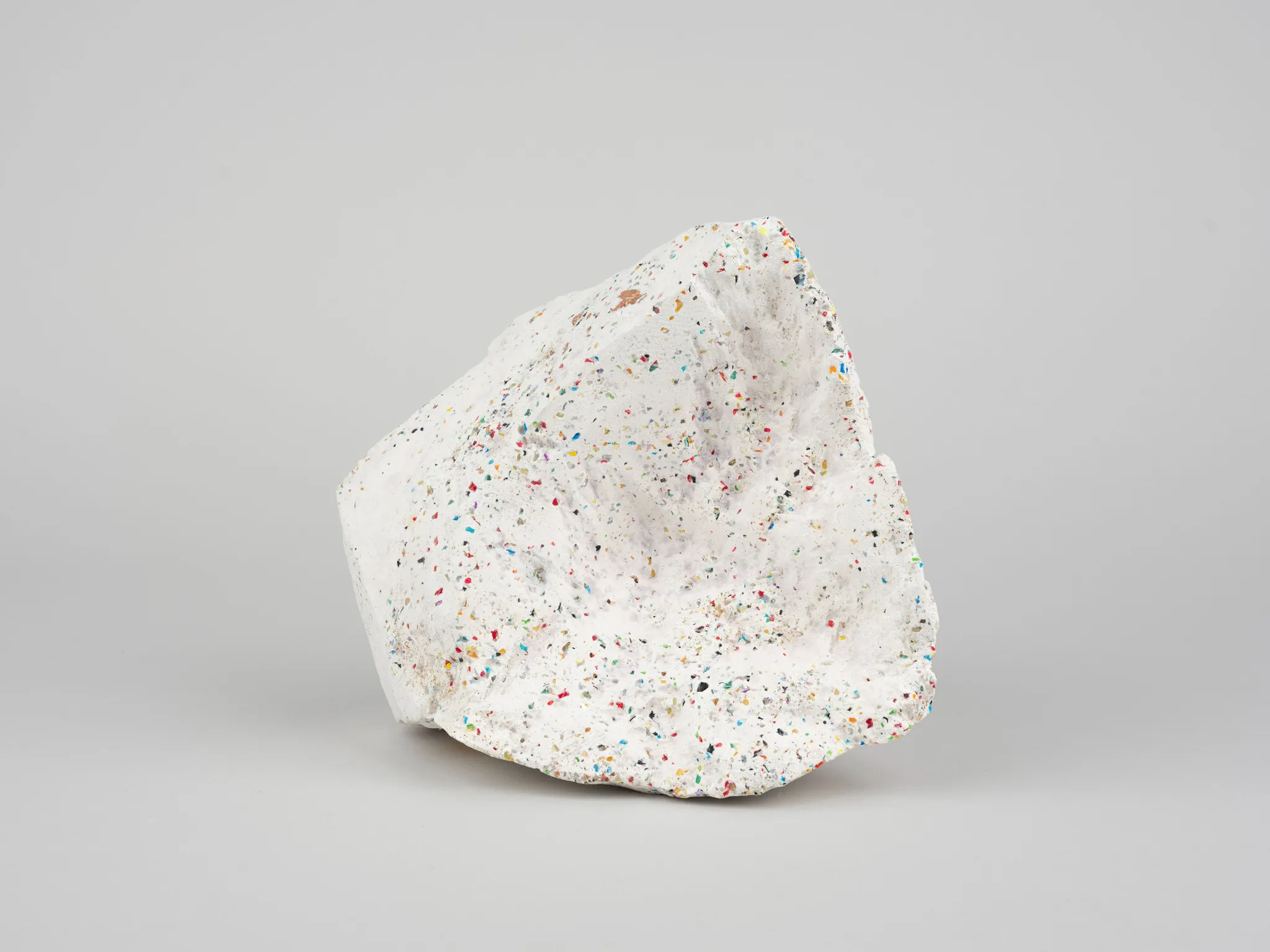 A white porous stone with colorful dots, photographed against a white background