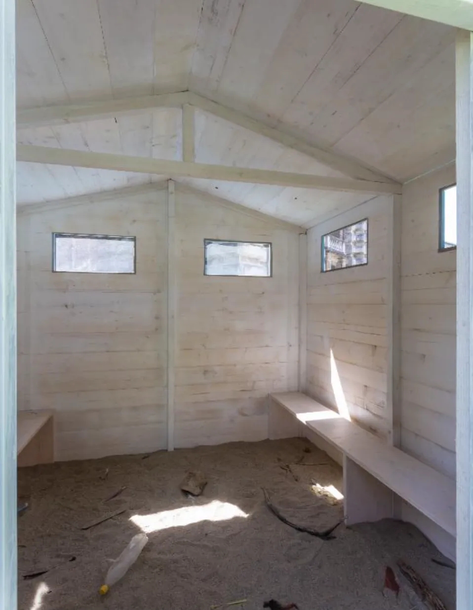 The inside of the wooden beach cabin with two wooden benches, sand and various sea debris on the floor