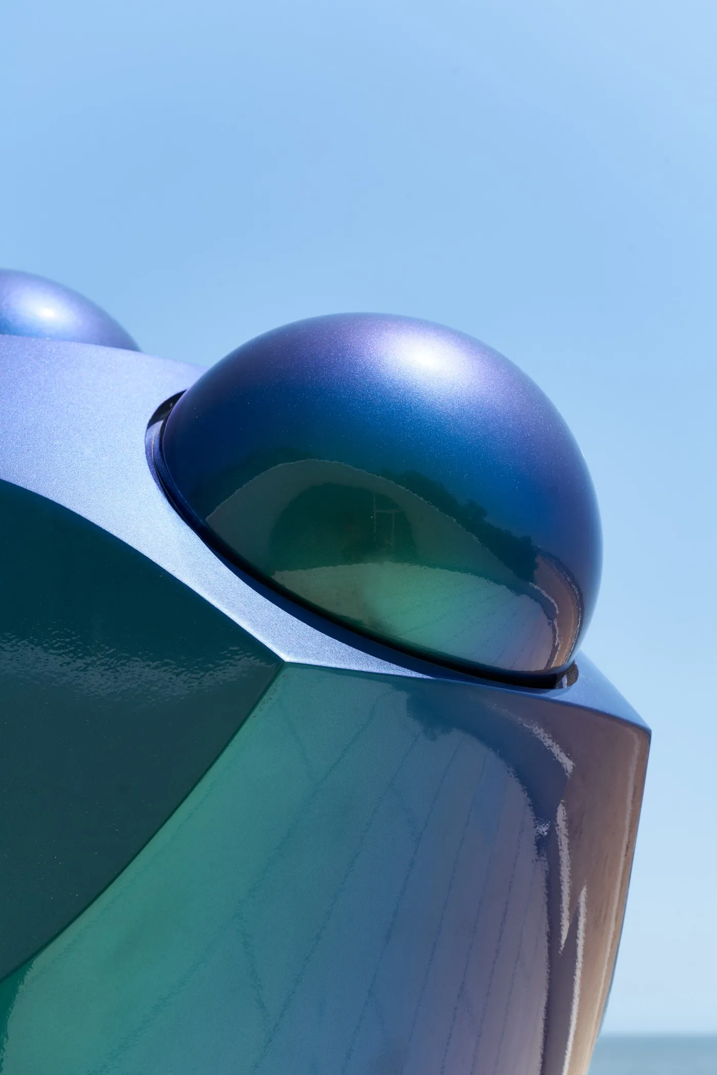 close up of the iridescent-coloured sculpture with reflection of the paved terrace